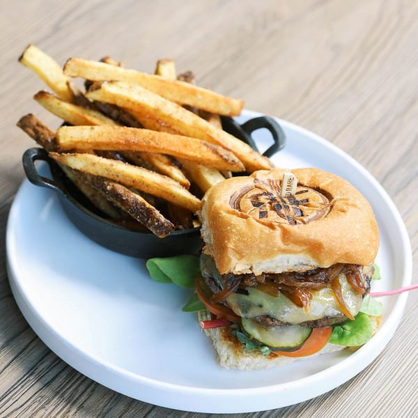 A Rustik Fork burger with caramelized onions, cheese, and pickles, served with a side of fries.