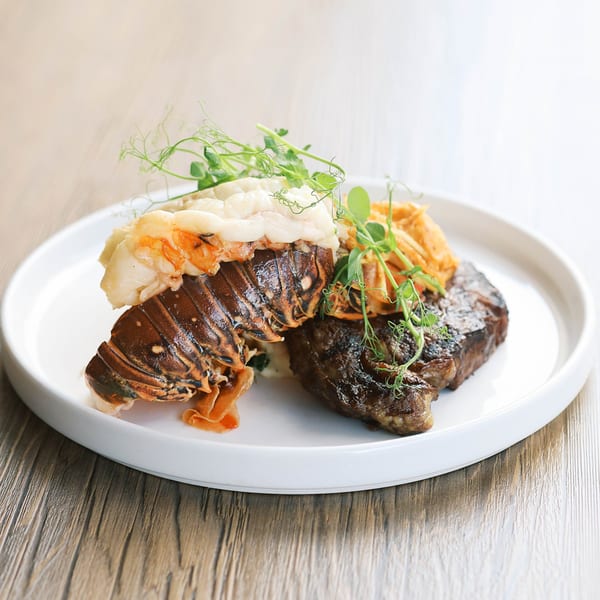 Grilled steak and lobster tail with microgreens and a side of sweet potato fries.