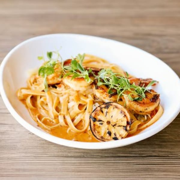 The Rustik Fork's shrimp pasta with grilled lemon and fresh herbs in a white bowl.
