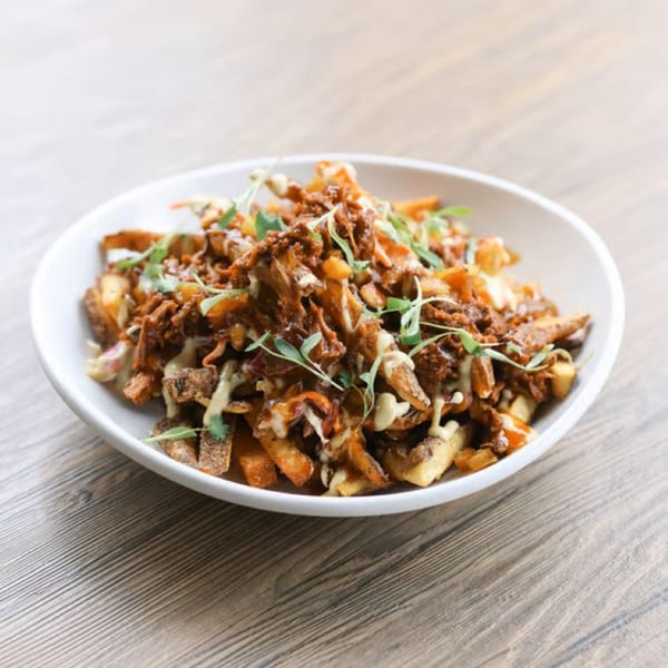 A white bowl of Rustik Fork's loaded fries with pulled pork, cheese sauce, and microgreens.