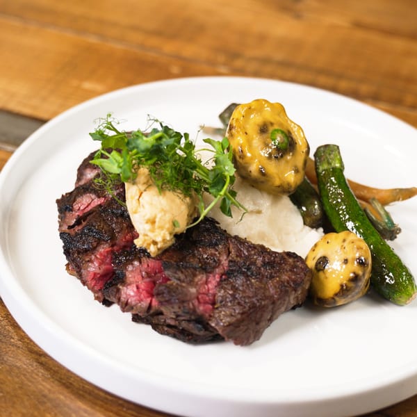 Grilled steak, mashed potatoes, roasted zucchini, and yellow squash, garnished with microgreens and a dollop of sauce.