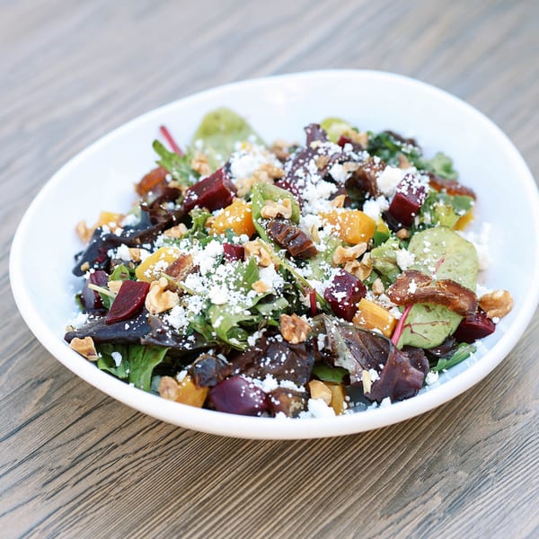 A vibrant beet and goat cheese salad with walnuts and mixed greens in a white bowl.